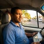 Eletricista brasileiro revisando documentos financeiros sobre desenquadramento MEI no tablet dentro da van de trabalho